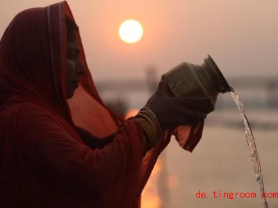  Diese gläubige Frau gießt Wasser aus einem Krug, um den So<em></em>nnengott und seine Frau anzubeten. F. Foto: Sunil Sharma/XinHua/dpa 
